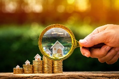 Magnifying Glass on a house sitting atop a stack of coins.