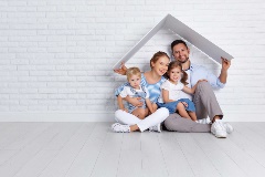 Happy Family sitting under a white abstracted roof shape, in front of a white brick wall.